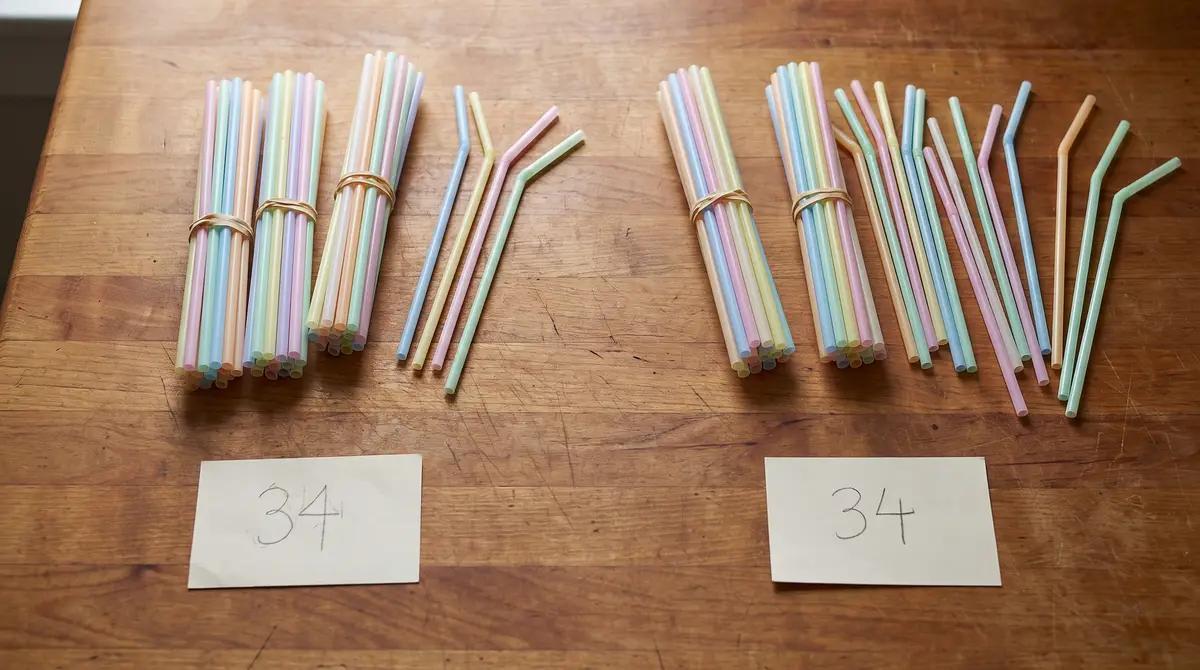 Two piles of drinking straws on a kitchen table, both labelled 34 — on the left three bundles of ten and four loose straws, on the right two bundles with the rest loose, showing regrouping in 2nd grade math